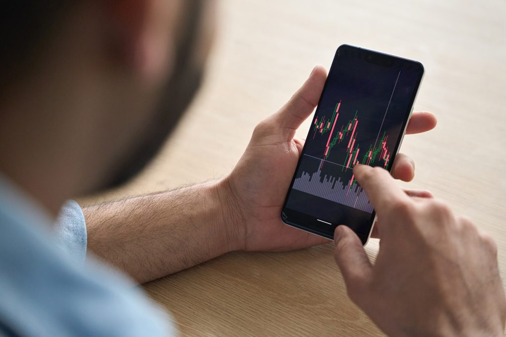 Closeup broker's hands holding cellphone with stockmarket and graphs.